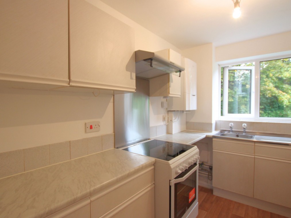 Modern kitchen interior featuring white cabinets, a gas stove, and a window with a view of greenery, highlighting the bright and airy atmosphere of the two-bedroom flat for rent at Rookley Court, Purfleet-On-Thames.