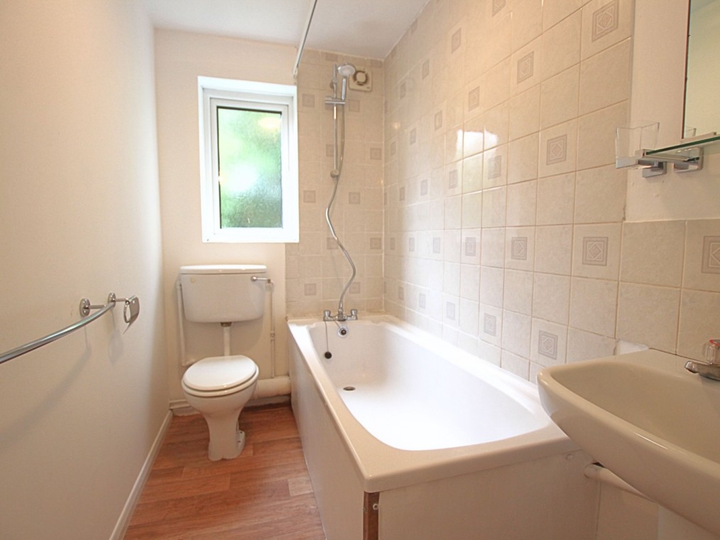Modern bathroom featuring a white bathtub, toilet, and sink, with tiled walls and a small window, showcasing the clean and functional design of the two-bedroom flat at Rookley Court, Purfleet-On-Thames.
